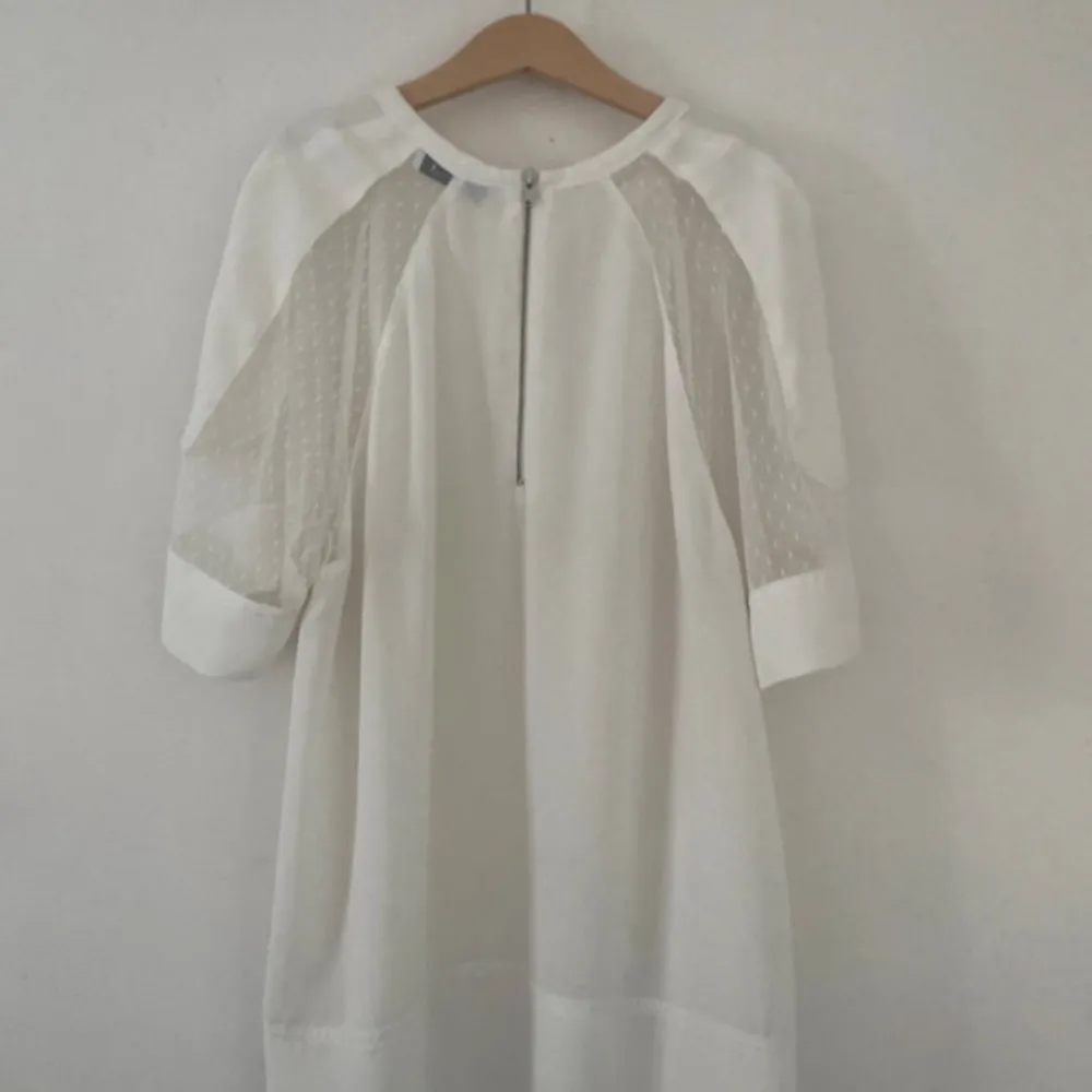 Elegant vit blus från Samsøe Samsøe med transparenta detaljer på ärmarna och dragkedja i ryggen. Blusen har korta ärmar och en rund halsringning, perfekt för en stilren look. Storlek S/M. Yläosat.