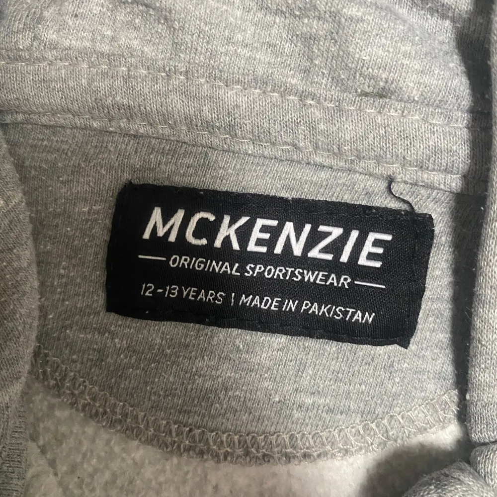 Säljer en grå hoodie från McKenzie med dragkedja framtill. Tröjan har en klassisk design med huva och långa ärmar, perfekt för en avslappnad stil. Tillverkad i mjukt material för extra komfort.. Neuletakit & Villapaidat.