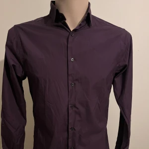 Lila skjorta från The Shirt Factory - Snygg lila skjorta från The Shirt Factory, designad av Linnea Braun. Skjortan har en extra slim fit passform och är lättstruken. Perfekt för en stilren look med knappar framtill och klassisk krage.