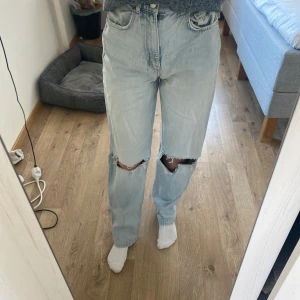 Ljusa high waist jeans med slitningar - Snygga ljusa high waist jeans från Gina Tricot med slitningar på knäna. De har en klassisk femficksdesign och knappgylf. Perfekta för en avslappnad stil.