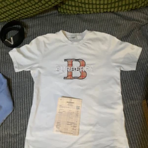 Burberry T-shirt med broderad logga. - Säljer min vita burberry T-shirt som jag har haft i ett halv år men bara använt ett fåtal gånger. Tröjan är i ett 9,5/10 skick. Den är inte 10 för att jag har använt den några gånger men den är som ny. Pris kan såklart diskuteras och om du har några funderingar så fråga gärna. Burberry kvittot följer med.