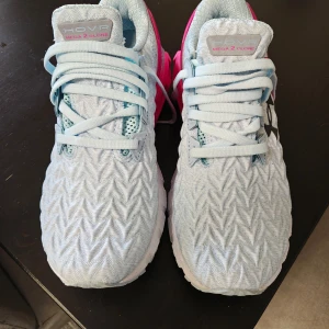 Under Armour HOVR Mega 2 Clone löparskor - Säljer ett par Under Armour HOVR Mega 2 Clone löparskor i ljusblått med rosa detaljer. Skorna har snörning och en unik mönstrad ovandel. Perfekta för löpning med bra dämpning och komfort. Provade, aldrig använda utomhus 