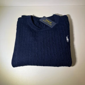 Mörkblå tröja från Polo Ralph Lauren - Säljer en stilren mörkblå tröja från Polo Ralph Lauren. Tröjan är stickad med en vit logga på brösten tröjan är helt ny säljer pga inte min still 