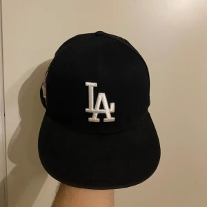 Svart keps med LA-broderi - Snygg svart keps från New Era med LA-broderi framtill och World Series 1981-märke på sidan. Perfekt för sportfantasten! Priset kan diskuteras där vi båda är glada