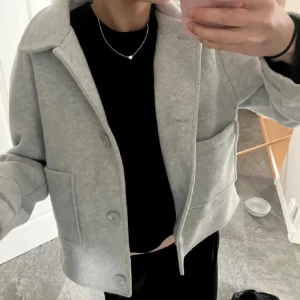 Grå kappa med knappar - Snygg grå kappa med stora knappar och bred krage. Jackan har en stilren design med raka linjer och stora fickor framtill. Perfekt för en stilren look.