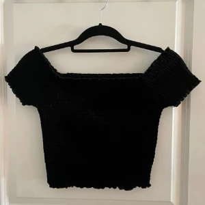 Svart offshoulder topp  - Snygg svart offshoulder topp från BikBok i storlek S. Toppen har en smockad design som ger en tight passform och korta ärmar. Perfekt för en stilren look. I ett fint skick ⭐️
