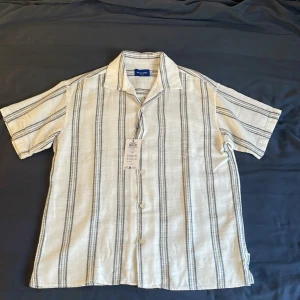 Sommar skjorta från Jack & Jones - Snygg kortärmad skjorta från Jack & Jones i vit med svarta ränder. Ej använd och lappen sitter kvar. Ny pris: 499kr