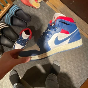 Nike Air Jordans i blått, vitt och rött - Snygga Nike Air Jordans i en fräsch färgkombination av blått, vitt och rött. Skorna har klassisk snörning och den ikoniska Air Jordan-loggan på sidan. Perfekta för dig som vill ha en stilren och sportig look.