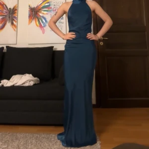 Mörkblå balklänning - Intressekoll! Elegant mörkblå långklänning med halterneck-design och öppen rygg. Klänningen har en figurnära passform som framhäver silhuetten. Perfekt för en speciell kväll! Etiketten är kvar och den är helt oanvänd. 