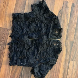 Svart spets topp med dragkedja - Snygg svart spets topp med ett unikt blommigt mönster. Toppen har en dragkedja baktill som ger en cool detalj. Perfekt för att lägga till en touch av elegans till din outfit.