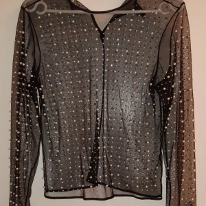Svart transparent topp med pärlor från H&M Divided - Snygg svart transparent topp från H&M Divided, dekorerad med pärlor. Toppen har långa ärmar och en elegant design som passar perfekt för en kväll ute.