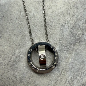 Halsband från Edblad med cirkel och sten - Elegant halsband från Edblad med en cirkelformad hängsmycke i silverfärg. Hängsmycket har en infälld klar sten i mitten och kedjan är tunn och stilren. Har aldrig använt det, men har inte kvar originalförpackningen.