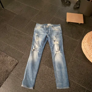  33 32 LjusBlå Jack and Jones slim fit jeans - Säljer ett par blå slimfit jeans med slitna detaljer och en fet tvätt. Strlk w 33 L 32