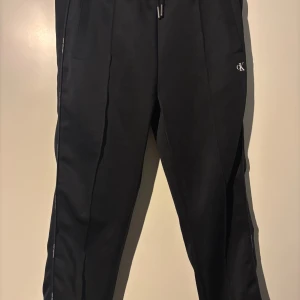 Calvin Klein byxor svarta - Snygga svarta byxor från Calvin Klein Jeans med diskret logga på sidan. Byxorna har en bekväm passform med snörning i midjan och sidofickor. Perfekta för en stilren look. Köps med tillhörande tröja för 699kr. Mycket bra skick. Barnstorlek, 160.