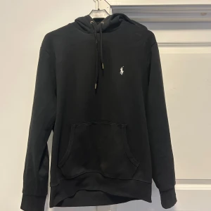 Svart hoodie från Ralph Lauren Medium - Säljer en stilren svart hoodie från Ralph Lauren med det klassiska logotypbroderiet på bröstet. Tröjan har en känguruficka och justerbar huva med snören. Perfekt för en avslappnad look. Jag är 177cm och väger 65 kg och den passar perfekt.