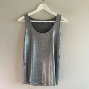 Silverfärgad glittrig linnetopp Kappahl - Snygg och glittrig silverfärgad linnetopp med rund halsringning. Perfekt för att lysa upp vilken outfit som helst. Supersnygg till både svart och vitt. Rensar garderoben så kika gärna på övriga annonser! 