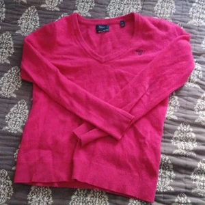 Röd ulltröja från Gant - Säljer en snygg röd ulltröja från Gant med v-ringning. Tröjan har långa ärmar och en broderad logga på bröstet. Perfekt för kyligare dagar!❤️ står storlek S men skulle säga xs🫶