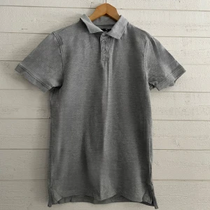 Grå pikétröja - Snygg grå pikétröja med klassisk krage och knappar framtill. Perfekt för en avslappnad stil. Kortärmad design som passar bra till både jeans och shorts.