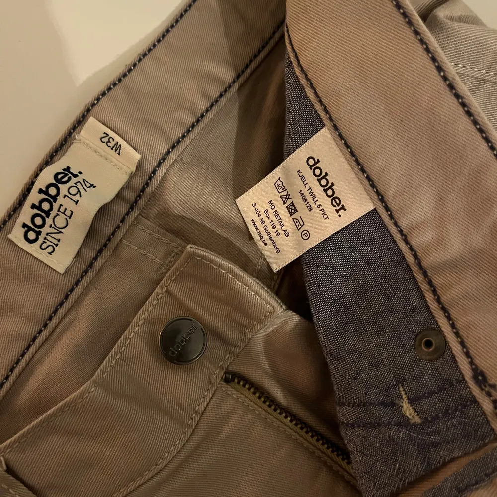 Snygga beige byxor från Dobber i storlek W32. De har en klassisk femficksdesign med knapp och dragkedja framtill. Perfekta för en stilren look.. Farkut & Housut.