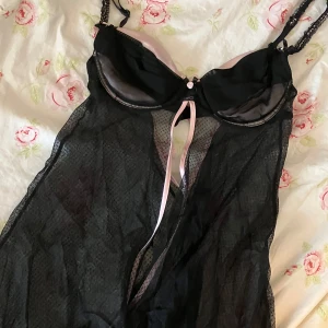 Svart spetstopp med rosa detaljer - svart spetstopp med rosa banddetaljer och dekorativ rosett framtill. har justerbara axelband och är genomskinlig!