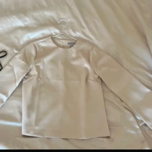 Beige långärmad blus  - Elegant beige blus med långa ärmar och rund halsringning. Blusen har en diskret dragkedja i ryggen. Perfekt för en stilren look.