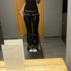 Svarta skinnbyxor - Snygga svarta skinnbyxor med bootcut-stil. De är lågmidjade och har en glansig finish som ger en cool look. Perfekta för att skapa en trendig outfit💕