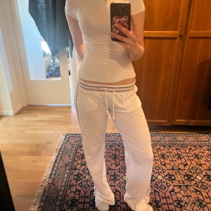 Vita mjukisbyxor från subdued - Säljer ett par vita mjukisbyxor med rosa sidopaneler och grå randig midja från subdued. Byxorna har en dragsko i midjan för justerbar passform och två bakfickor. Byxorna påminner av  2000s. Priset kan diskuteras💕🥰