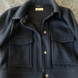 Mörkblå jacka från Esprit - Snygg mörkblå jacka från Esprit med knappar framtill och två stora fickor. Perfekt för höst och vår. Klassisk design med krage och långärmad stil.