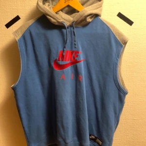 Blå och grå ärmlös hoodie från Nike - Säljer en cool ärmlös hoodie från Nike i blått och grått. Den har en stor röd Nike Air-logga på framsidan och en praktisk huva. inga defekter Passar M-L . Pris kan diskutera