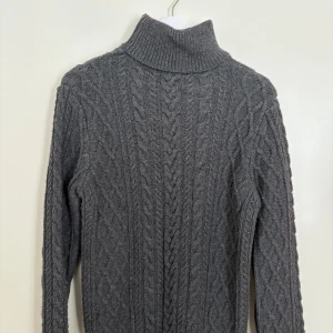 Grå stickad polotröja - Säljer en mysig grå stickad polotröja med kabelstickat mönster. Tröjan har långa ärmar och en hög krage som håller dig varm under kyliga dagar. Perfekt för höst och vinter!