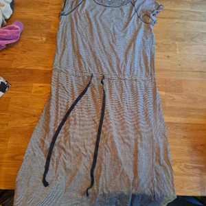 Randig klänning från Hampton Republic - Säljer en randig klänning från Hampton Republic i blått och vitt. Klänningen har en knytning i midjan och är ärmlös, perfekt för en avslappnad stil. Den är gjord i ett mjukt och bekvämt material.