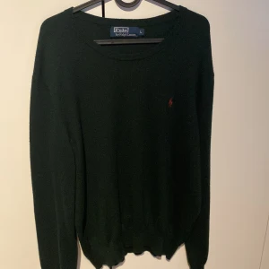 Mörkgrön tröja från Polo Ralph Lauren - Säljer en stilren mörkgrön tröja från Polo Ralph Lauren med det klassiska röda logotypbroderiet på bröstet. Tröjan har långa ärmar och en rund halsringning, perfekt för en elegant och avslappnad look. Andvänd ett tiotal gånger 
