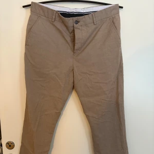 Beige chinos med knappar - Snygga beige chinos med knappar och dragkedja. Perfekta för en stilren look. De har en normal passform och är tillverkade i ett bekvämt bomullsmaterial. Storlek Eu 48