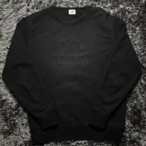 Svart sweatshirt från C.P. Company - Snygg svart sweatshirt från C.P. Company med broderad logga på bröstet. Tröjan är i mycket bra skick och går för 3000 tusen ny. Skick 9/10, storleken är L men sitter perfekt som en m. Diskutera pris i dm. 