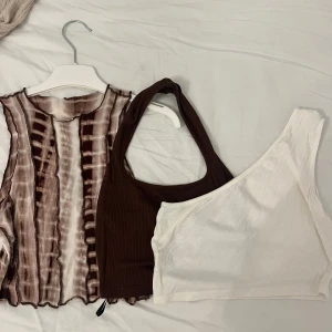 Tre toppar - paketpris  - Säljer tre snygga toppar: en ärmlös brun- och vitrandig blus med vågig kant, en brun ribbad oneshoulder-topp och en vit ribbad oneshoulder-topp.  1st - 50kr 2st - 80kr 3st - 120kr