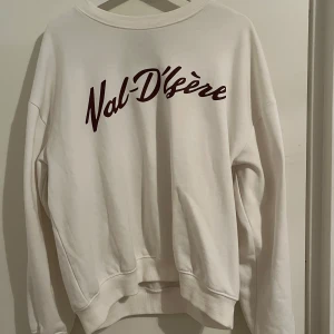 Vit sweatshirt från 157 - Säljer en vit sweatshirt från 157 med texten 'Val-D'Isère' i vinrött på framsidan. Tröjan har en klassisk rund hals och långa ärmar. Perfekt för en avslappnad stil.