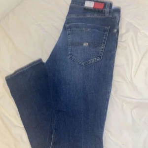 Blå jeansbyxor från Tommy Hilfiger - Snygga blå jeansbyxor från Tommy Hilfiger i slim fit. De har en klassisk femficksdesign och en knappgylf. Perfekta för en stilren look.