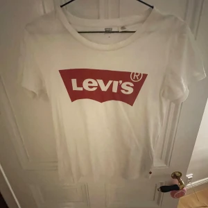 Vit t-shirt från Levi's - Säljer en klassisk vit t-shirt från Levi's med det ikoniska röda logotyptrycket på framsidan. T-shirten har en rund hals och korta ärmar, perfekt  för en avslappnad stil. Står strl xs men passar mig bra som är strl s.