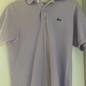 Ljuslila pikétröja från Lacoste - Tja, säljer nu min snygga ljuslila pikétröja från Lacoste med klassisk krage och knappar framtill. Den har korta ärmar och det ikoniska gröna krokodilemblem på bröstet. Perfekt för en stilren och avslappnad look. Tveka inte på att höra av er vid funderingar! Mvh Sixten 
