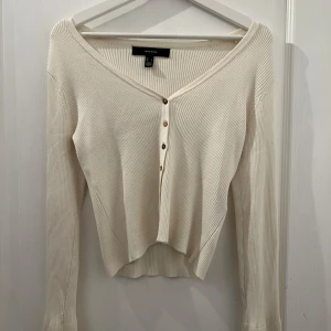 Vit ribbad kofta från Vero Moda - Säljer en stilren vit ribbad kofta från Vero Moda. Koftan har en v-ringad design med knappar framtill och långa ärmar. Perfekt för en avslappnad och chic look.