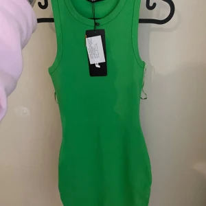 Grön ribbad klänning från New yorker - Snygg grön ribbad klänning från New yorker i en tight passform. Klänningen är ärmlös och perfekt för en stilren look. Den har en enkel design som gör den lätt att matcha med olika accessoarer.