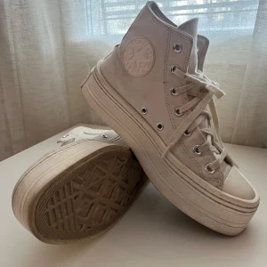 Vita höga sneakers från Converse - Säljer ett par vita höga Converse sneakers med platåsula. Skorna har klassisk snörning och Converse-logga på sidan. Perfekta för en stilren look.