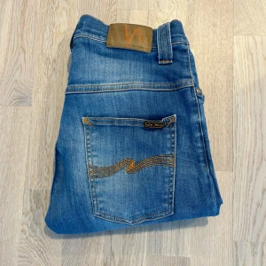 Blå Nudie Jeans - Snygga blå jeans från Nudie Jeans med klassisk femficksdesign och en trendig look. De har en Slim passform. Märkets ikoniska broderi syns på bakfickorna. Storlek 29/32. Modell: Thin Finn (passar Slim)