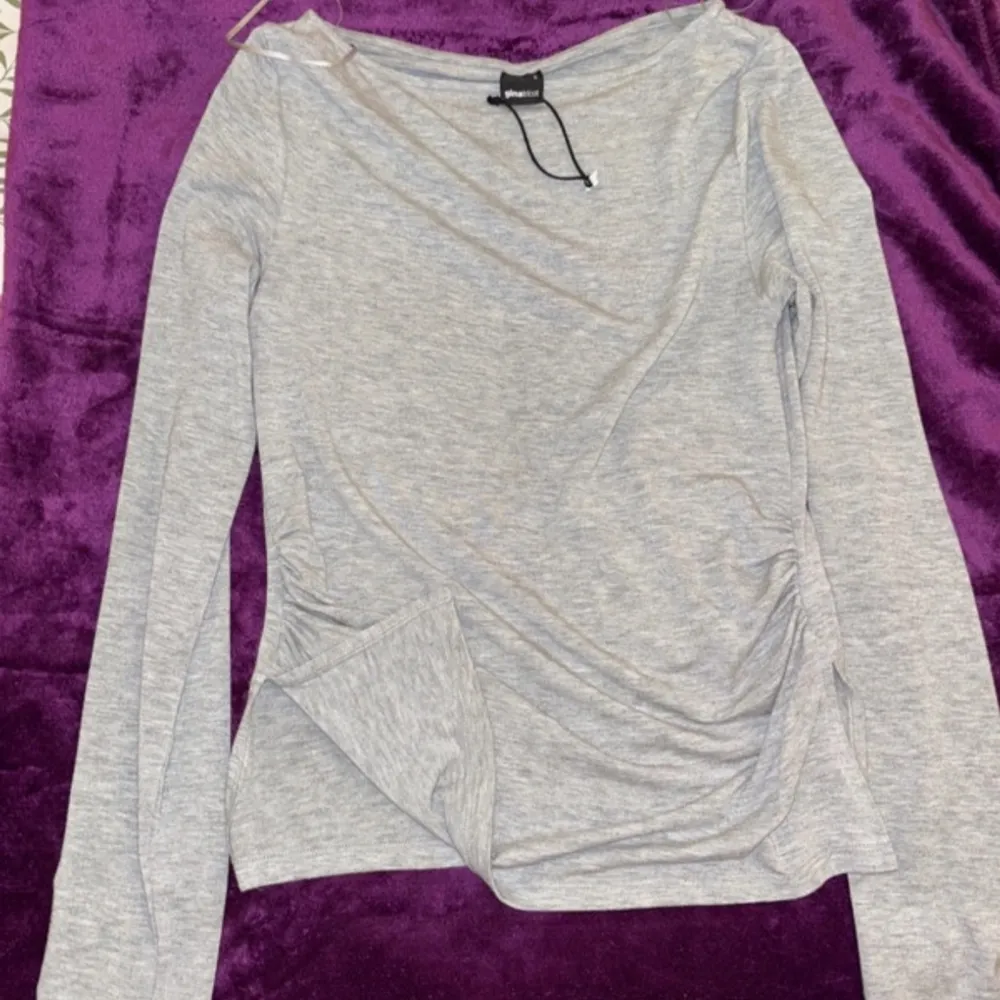 Säljer en stilren grå långärmad topp från Gina Tricot. Toppen har en enkel design med en liten slits på sidan och är perfekt för en avslappnad look. Materialet är mjukt och bekvämt.. Neuletakit & Villapaidat.