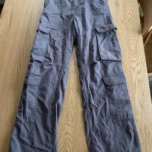 Grå cargobyxor från Bershka - Säljer ett par grå cargobyxor från Bershka med flera praktiska fickor och dragkedja. De har även snörning i midjan för att kunna ”forma figuren” mer - men de sitter fint utan det också. Använd 1 gång så verkligen som nya!