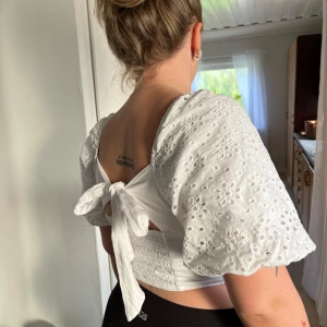 Vit blus med puffärmar och knytning - Säljer en superfin vit blus med puffiga ärmar och snygg knytning i ryggen. Den har ett vackert broderat mönster och är perfekt för sommardagar. Blusen är croppad och ger en söt och stilren look.