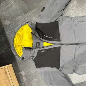Grå och gul jacka från Sail Racing - Säljer en grå och gul jacka från Sail Racing. Den har en cool design med svart detaljer och en ljusgul insida som verkligen poppar. Jackan har dragkedja framtill och flera praktiska fickor med dragkedjor. Perfekt för kalla dagar med sin pufferstil och varma foder.