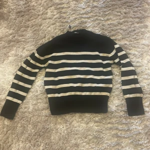 Randig stickad tröja från Gina Tricot - Säljer en superfin randig tröja från Gina Tricot. Den är svart med vita ränder och har en klassisk rund hals. Perfekt för både höst och vinter, och den är riktigt mysig att ha på sig. Tröjan är långärmad och gjord i ett mjukt stickat material. Passar