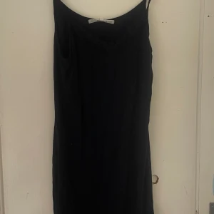 Svart klänning från RoseBud - Säljer en elegant svart klänning från RoseBud i storlek L. Klänningen har en enkel och stilren design, perfekt för festliga tillfällen. Den är ärmlös och har en smickrande passform. Perfekt för en kväll ute eller en speciell tillställning.