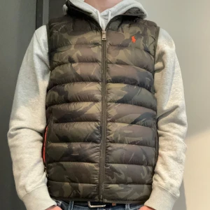 Polo Ralph lauren Väst - Raffe väst i snygg camo färg med orange inuti skick 9/10 väldigt sparsamt använd  Inga defekter eller liknande!  Tveka inte på att höra av er!